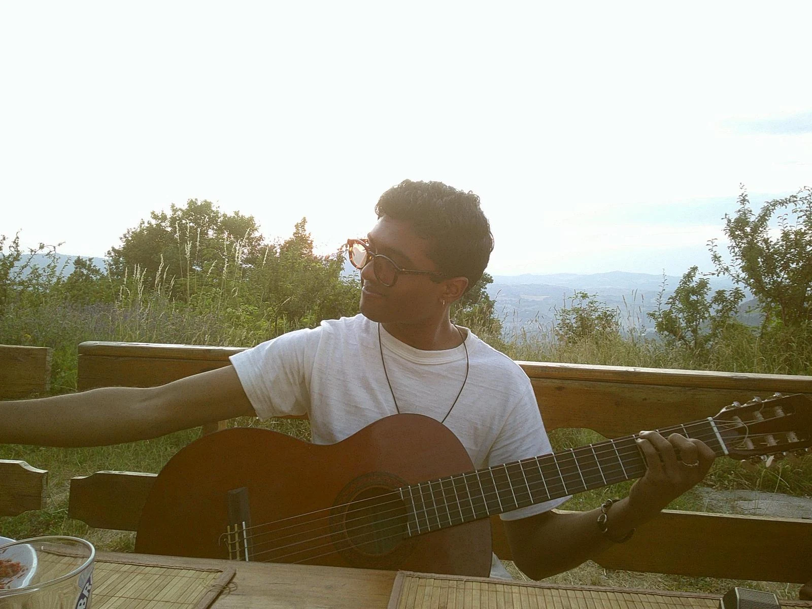 A musician playing acoustic guitar on a wooden deck overlooking a vast green landscape