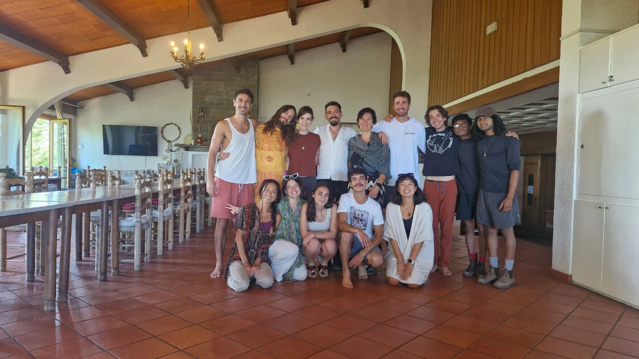 Fifteen Honeydew members of mixed ages gathered in a light-filled communal hall with wooden beams at Maiolo