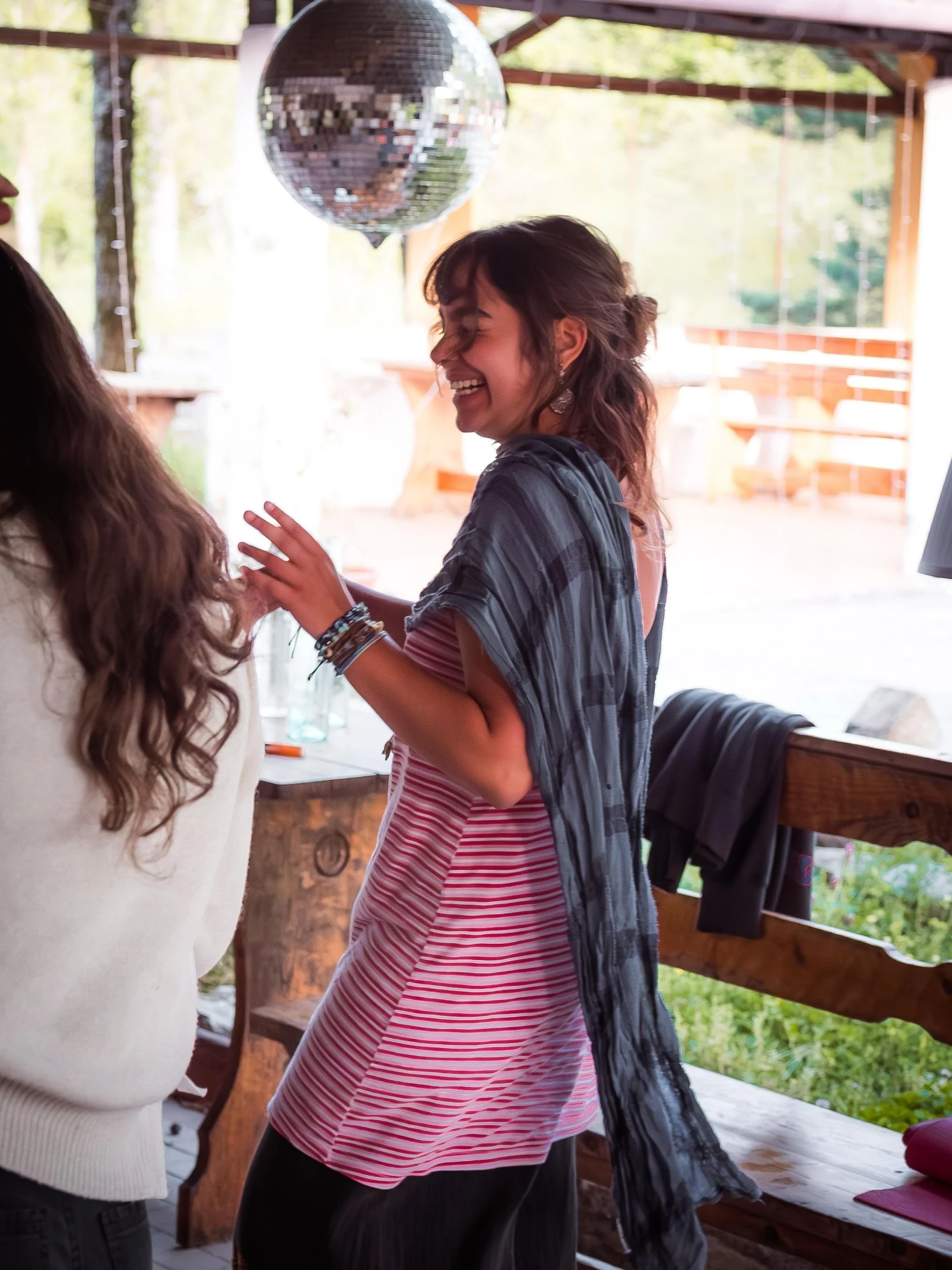 Two women laughing and dancing under a hanging disco ball on a covered wooden porch