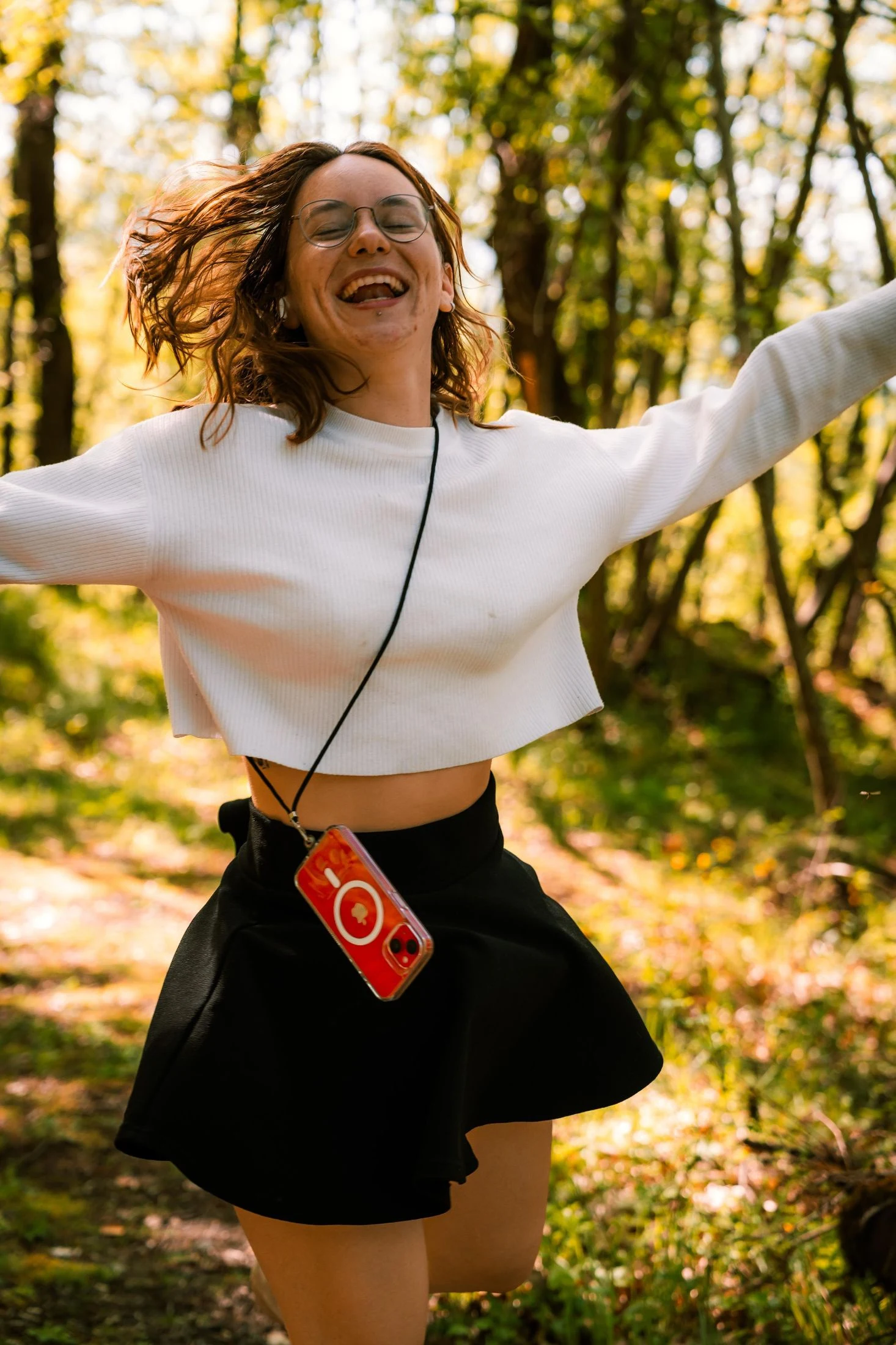 A young woman leaping joyfully with arms raised in a sunlit forest clearing